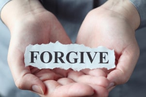 Torn piece of paper with the word "Forgive" in the woman's palms.